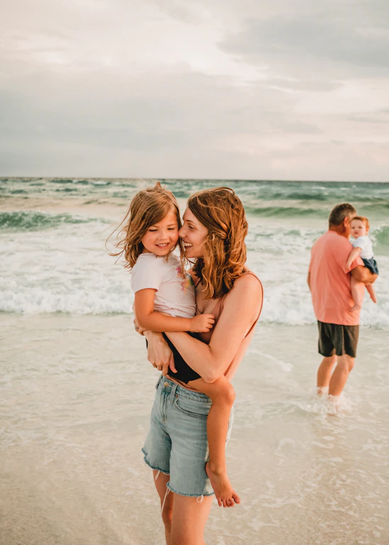 a woman holding a toddler on a beach