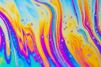 Vivid patterns of swirling colors resembling a psychedelic or abstract art piece, with waves of blue, orange, pink, and yellow blending seamlessly together. Small circular shapes are dispersed throughout, creating an intricate and lively design.
