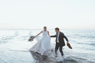 a man and woman in wedding attire running in water
