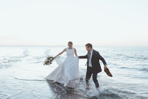 a man and woman in wedding attire running in water