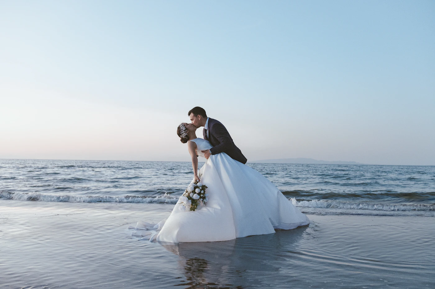 Cost-saving tips for destination weddings — A couple exchanges vows on a sandy beach at sunset.