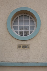 A round window with a light blue frame set into a textured beige wall. Behind the window, small model ships are visible. Below the window, a rectangular sign reads 'LES ONDINES'. The overall appearance is clean and nautical.