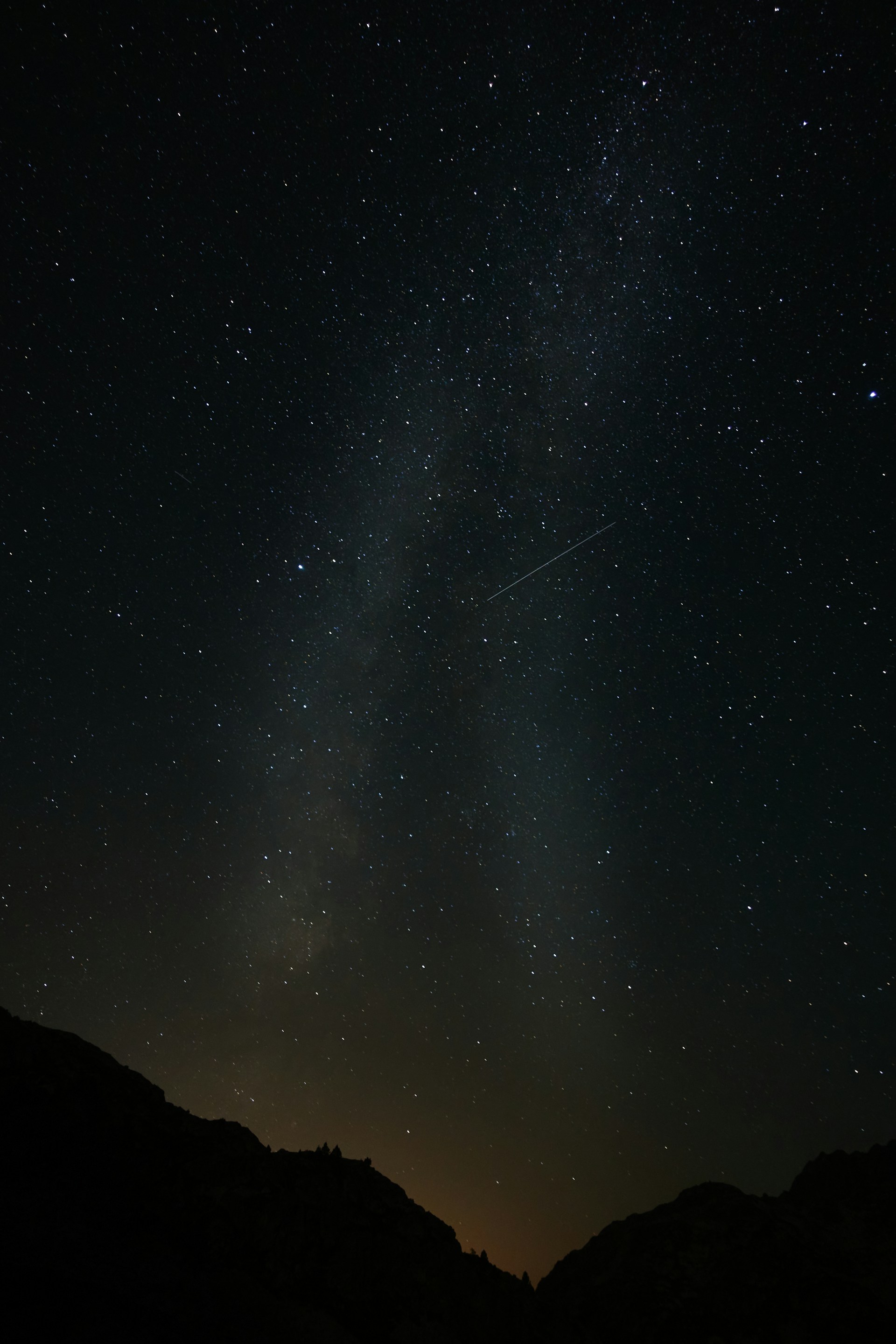 a starry night sky with a mountain and a jet trail