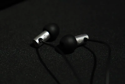 Sleek TC4 titanium alloy shell of the in-ear monitor resting on a deep black surface with subtle gold accents.