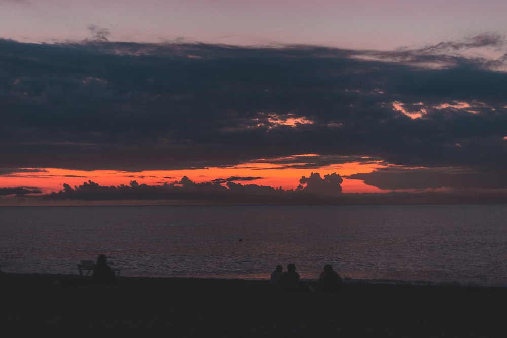 a group of people sitting on a beach at sunset