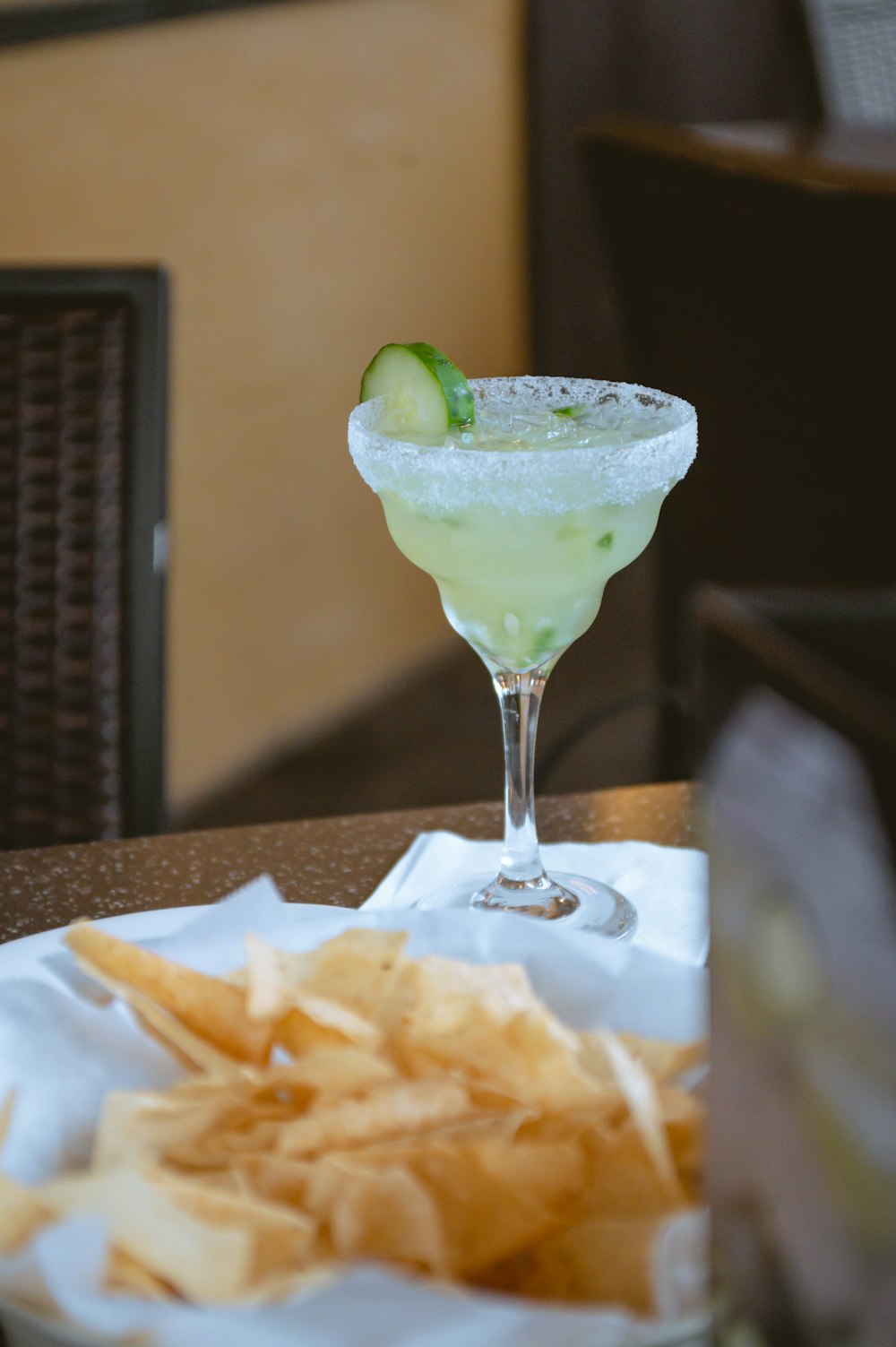 a glass of green liquid with chips and a slice of lime on a plate