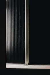 A dark, minimalist setting with vertical ridged lines and a narrow beam of light penetrating the darkness, highlighting a portion of the surface.