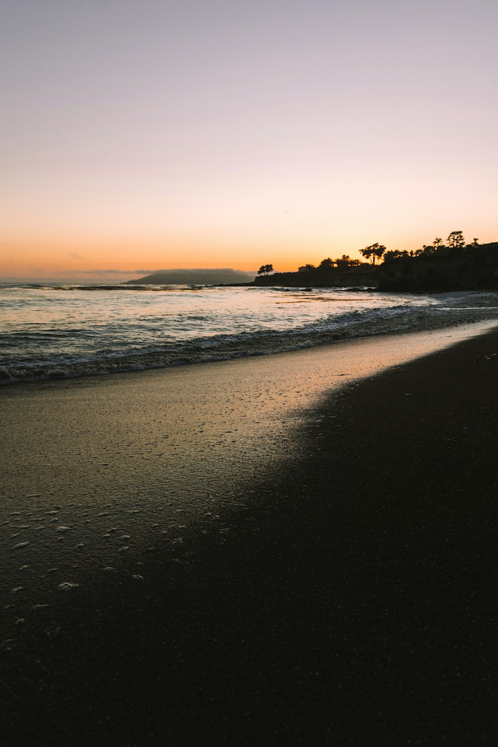 a beach with a body of water and a hill in the background