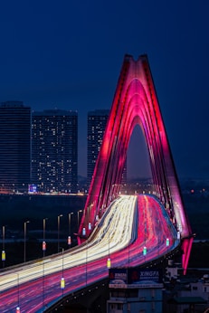 a bridge with a red and white design in front of a city