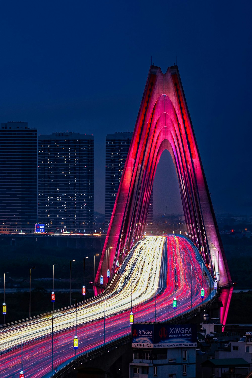 a bridge with a red and white design in front of a city