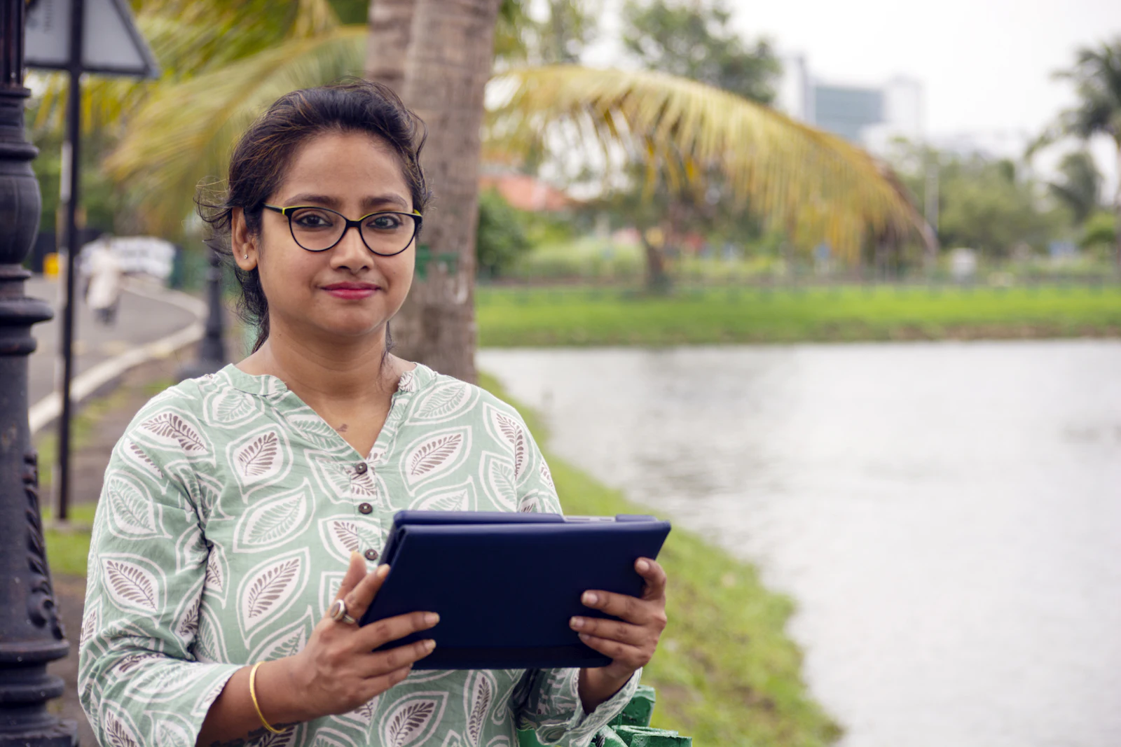 A young woman holding a tablet outdoors beside a lake