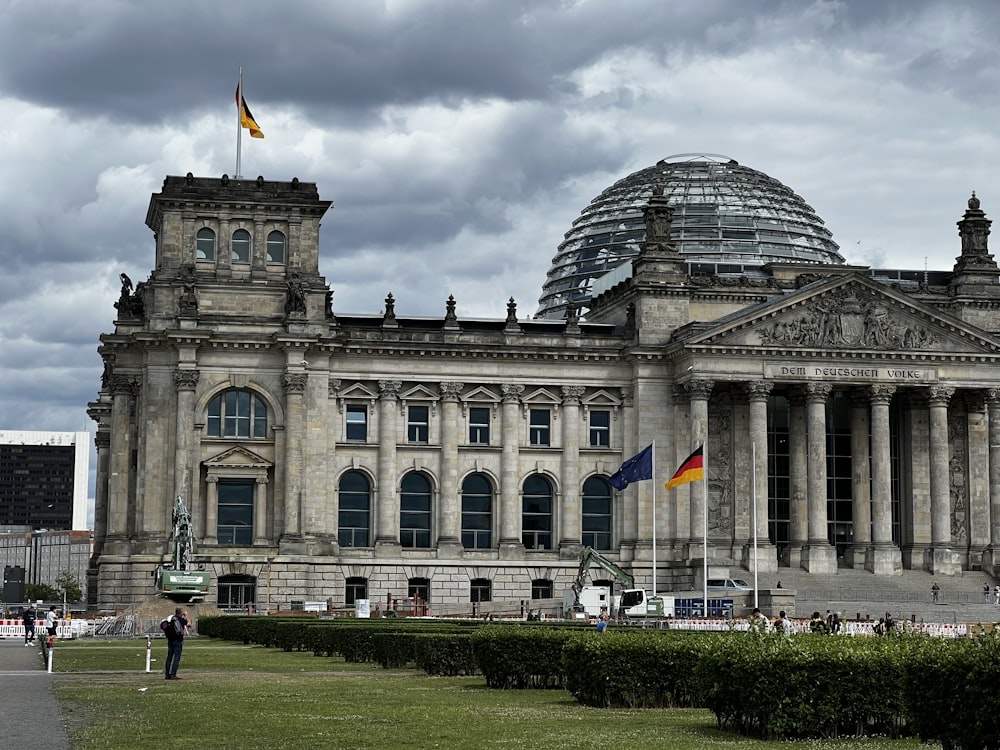 un grand bâtiment avec un dôme et des drapeaux devant lui avec le bâtiment du Reichstag en arrière-plan