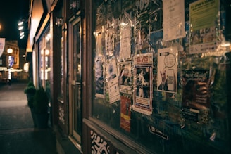 A vibrant urban street scene at night with black-themed event posters glowing under city lights.