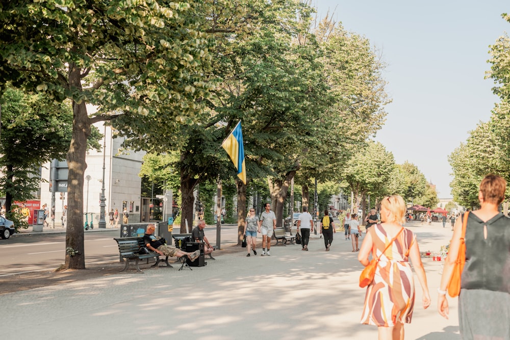 a person in a dress walking down a street with people and trees