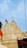The image features a traditional Indian temple with intricately carved spires and domes, adorned with orange flags. The temple is painted in a light cream color against a clear blue sky.