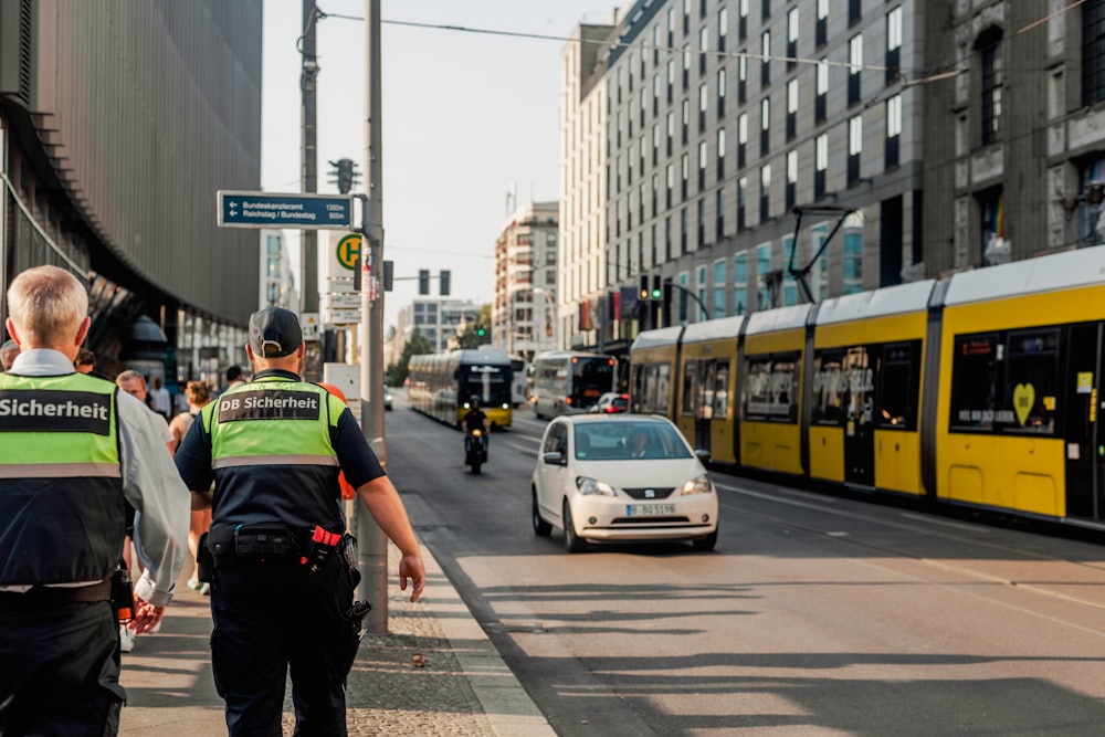 uma pessoa em um colete amarelo em pé na calçada ao lado de um carro e um ônibus