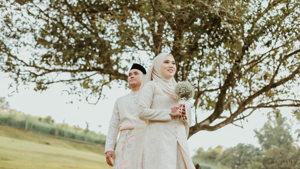 a man and woman in wedding attire standing under a tree