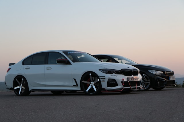 A sleek motorcycle and a shiny car parked side by side on an open road at sunset.