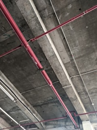A concrete ceiling with exposed red and white pipes running across its surface, showing an industrial or unfinished construction style.
