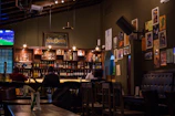 A cozy corner of the wine bar showing bottles lined up on shelves, a TV in the background showing a sports game.