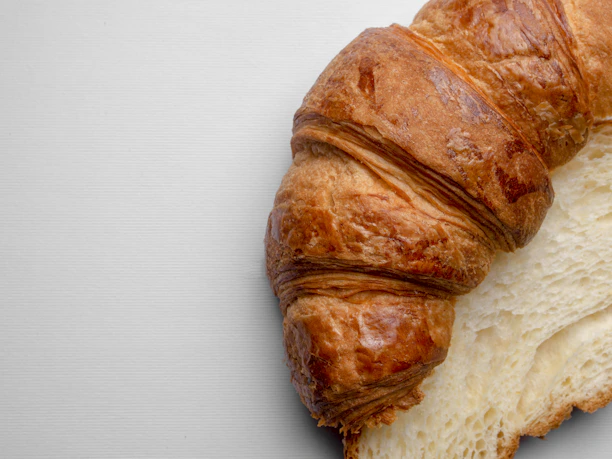 Close-up of a freshly baked golden croissant on a rustic wooden table.