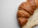 Close-up of a golden, flaky croissant resting on a rustic wooden table with soft morning light.
