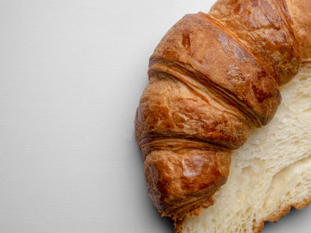 Close-up of a golden vanilla bean croissant with flaky layers on a rustic wooden board