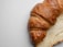 A close-up of a flaky croissant on a wooden table with a soft focus background.