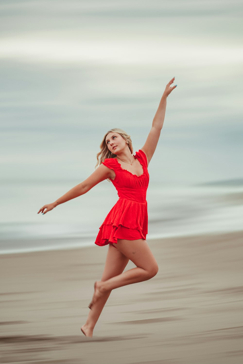 a woman in a red dress jumping on a beach