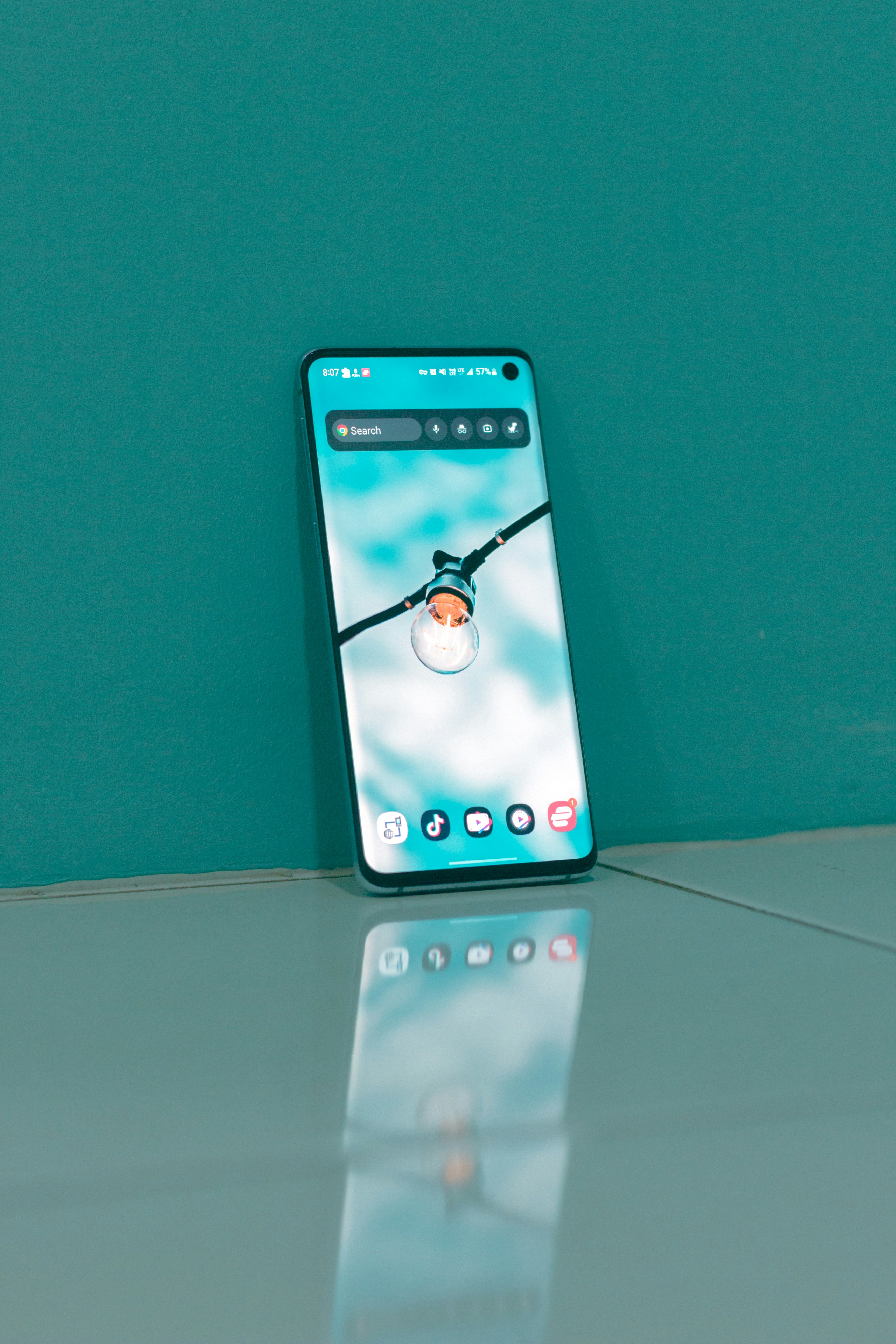 Smartphone with lightbulb wallpaper leaning against a teal wall.