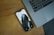 A smartphone with a black and white lock screen image of a person partially obscured by their hair is lying on a wooden surface beside a laptop keyboard.