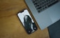 A smartphone with a black and white lock screen image of a person partially obscured by their hair is lying on a wooden surface beside a laptop keyboard.