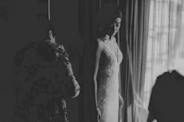 An intimate scene of a woman in elegant sleepwear standing by a window with sheer curtains.