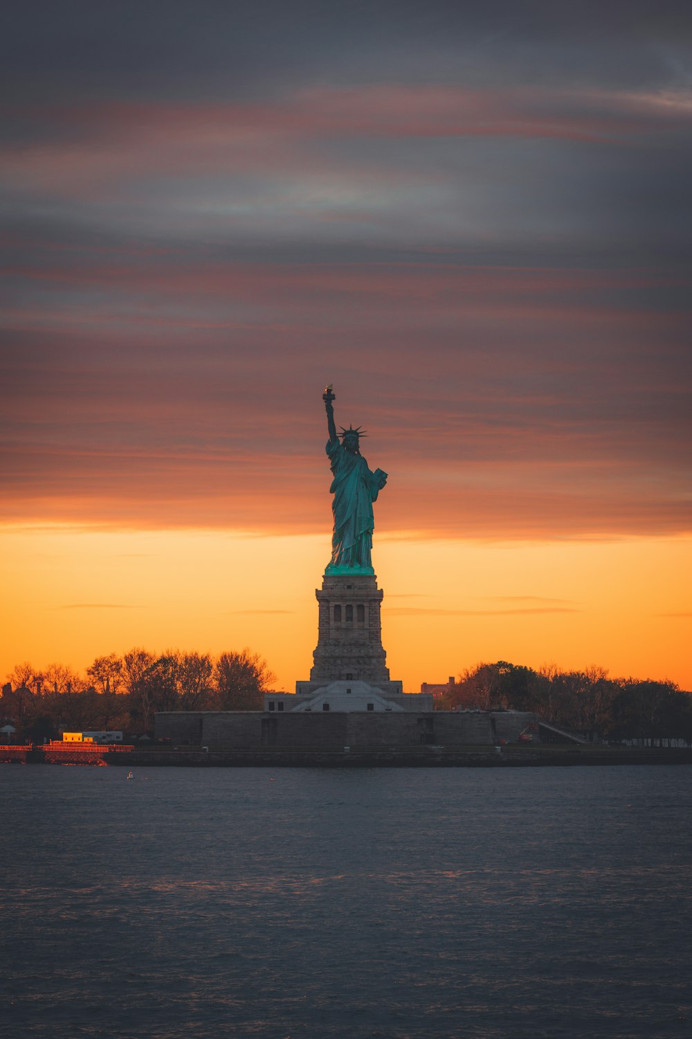 a statue of a person holding a torch in front of a sunset