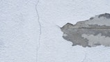 A textured wall with a noticeable crack running from top to bottom, alongside a large area where the plaster is peeling away to reveal the underlying concrete.