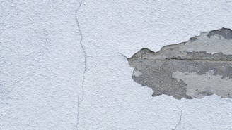 A textured wall with a noticeable crack running from top to bottom, alongside a large area where the plaster is peeling away to reveal the underlying concrete.
