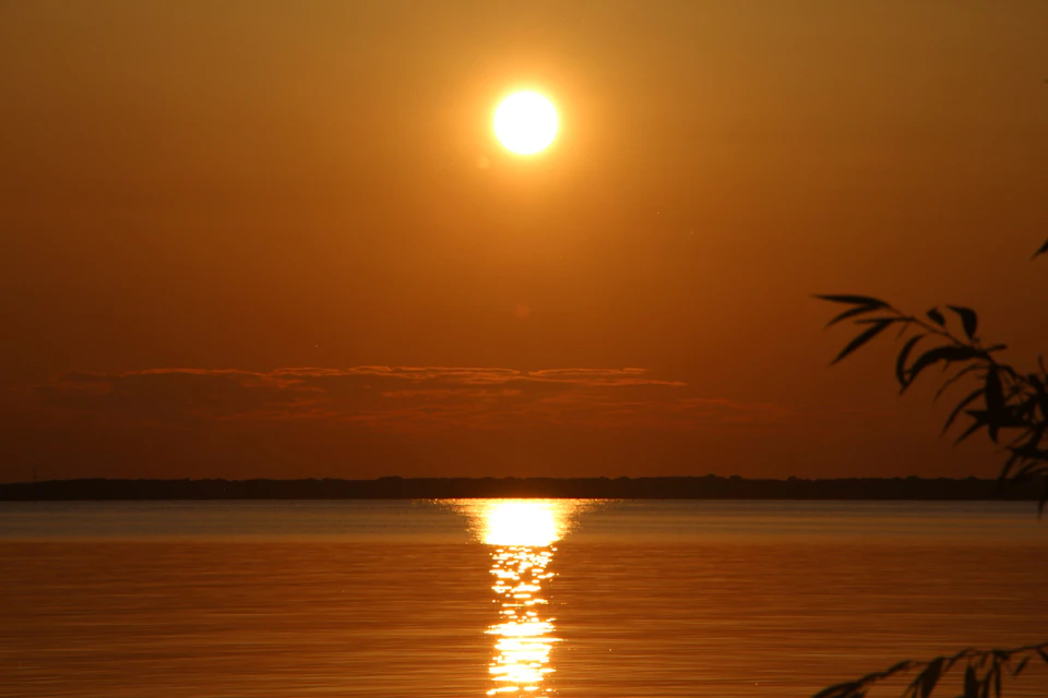 Serene sunset over water with sun casting warm glow behind horizon in orange hues