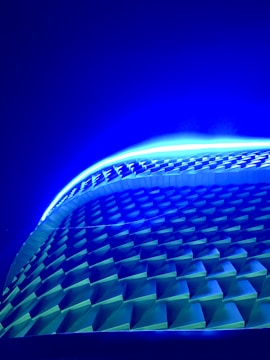 A series of geometric patterns arranged in a wave-like structure, illuminated by vibrant blue and green lighting, creating a futuristic and dynamic aesthetic.