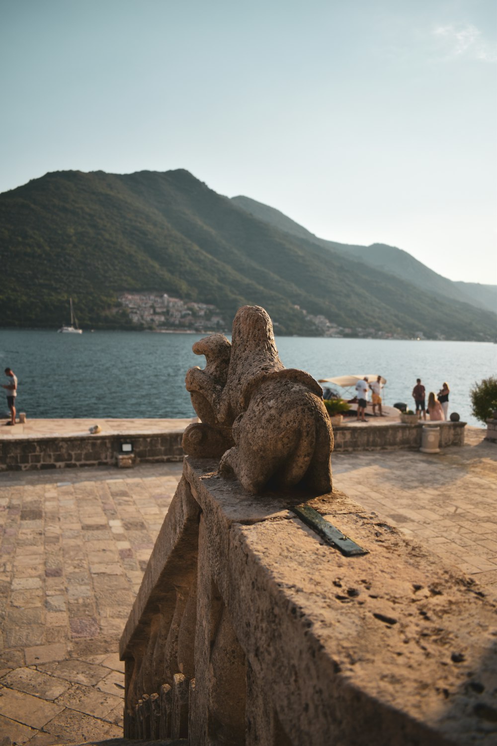 a stone statue on a stone wall overlooking a body of water