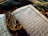 An open Arabic book with intricate calligraphy lying on a decorative fabric. A string of black prayer beads with tassels is placed across the pages, adding a contrast against the white and blue pages of the book.
