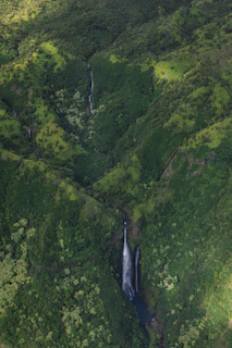 A scenic view of lush green hills and waterfalls cascading into natural pools on Pulau Peling