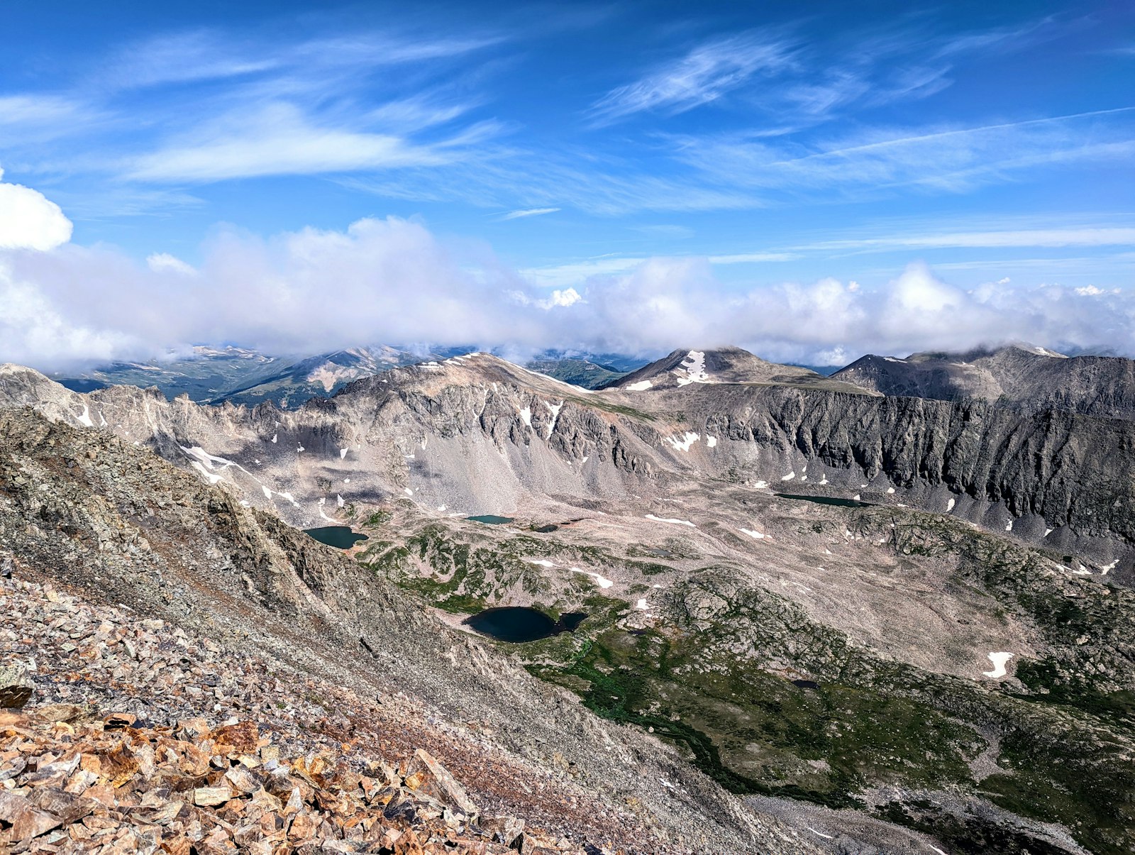 A rocky alpine ridge descending toward small turquoise lakes in a high mountain basin ringed by grey peaks