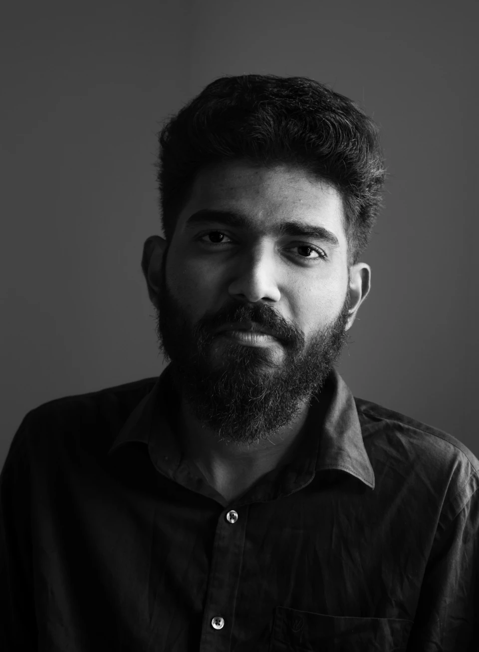 Man in black shirt with beard and mustache looks directly at the camera