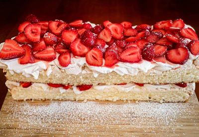 A freshly baked vanilla sponge cake topped with fresh strawberries and powdered sugar.