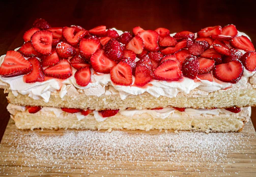 A rustic vanilla sponge cake topped with fresh strawberries and cream on a wooden table.