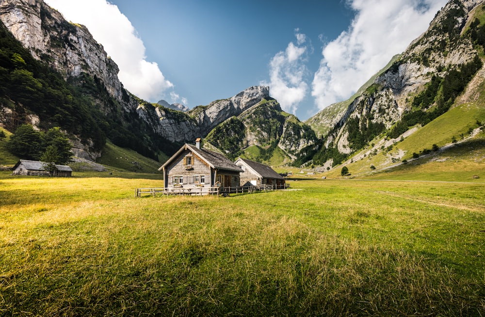 Una casa en un campo cubierto de hierba con montañas al fondo