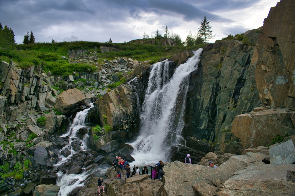 a group of people standing on rocks by a waterfall