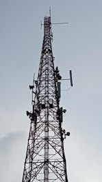 A tall, metal communication tower with multiple antennas and dishes attached, stretching vertically into the sky against a backdrop of a cloudy sky.