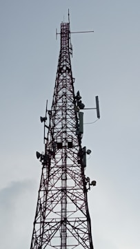 A tall, metal communication tower with multiple antennas and dishes attached, stretching vertically into the sky against a backdrop of a cloudy sky.