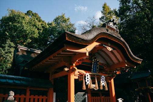 A traditional Japanese shrine with a beautifully curved roof surrounded by lush green trees. The structure is adorned with decorative elements and hanging ornaments, creating an atmosphere of serenity and tradition.
